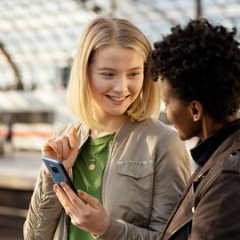 Kundinnen der DB mit einem Handy auf dem Bahnsteig am Hauptbahnhof Berlin. | © DB AG / Max Lautenschläger