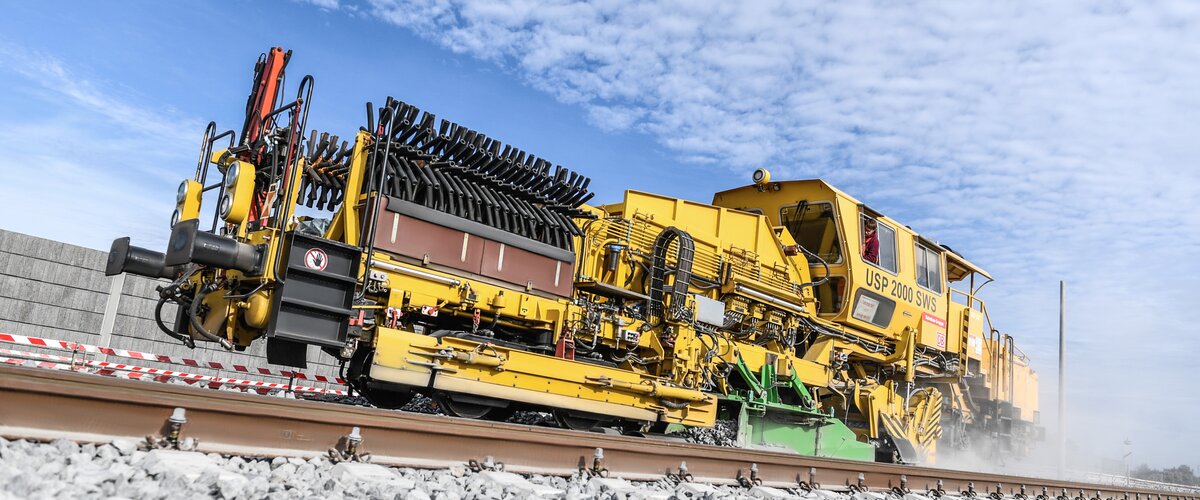 Ein Baustellenfahrzeug der Deutschen Bahn fährt vor blauem Himmel über die Schiene.  | © DB AG / Max Lautenschläger