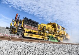 Ein Baustellenfahrzeug der Deutschen Bahn fährt vor blauem Himmel über die Schiene. 