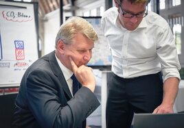 Zwei Männer im Büro schauen interessiert auf einen Bildschirm. 