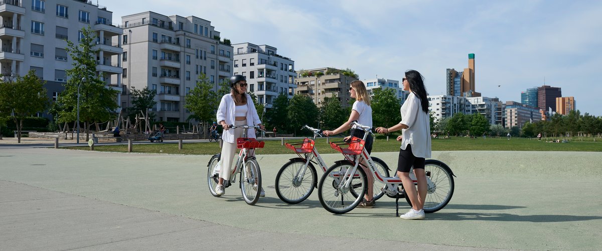 Drei Frauen begrüßen sich in einem Park, jede hat ein Fahrrad der Call a Bike-Initiative dabei. | © Deutsche Bahn AG / Faruk Hosseini