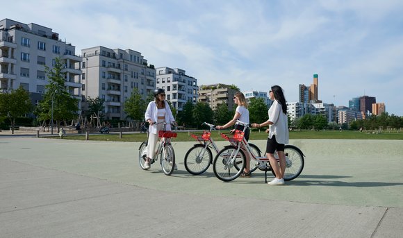 Drei Frauen begrüßen sich in einem Park, jede hat ein Fahrrad der Call a Bike-Initiative dabei.