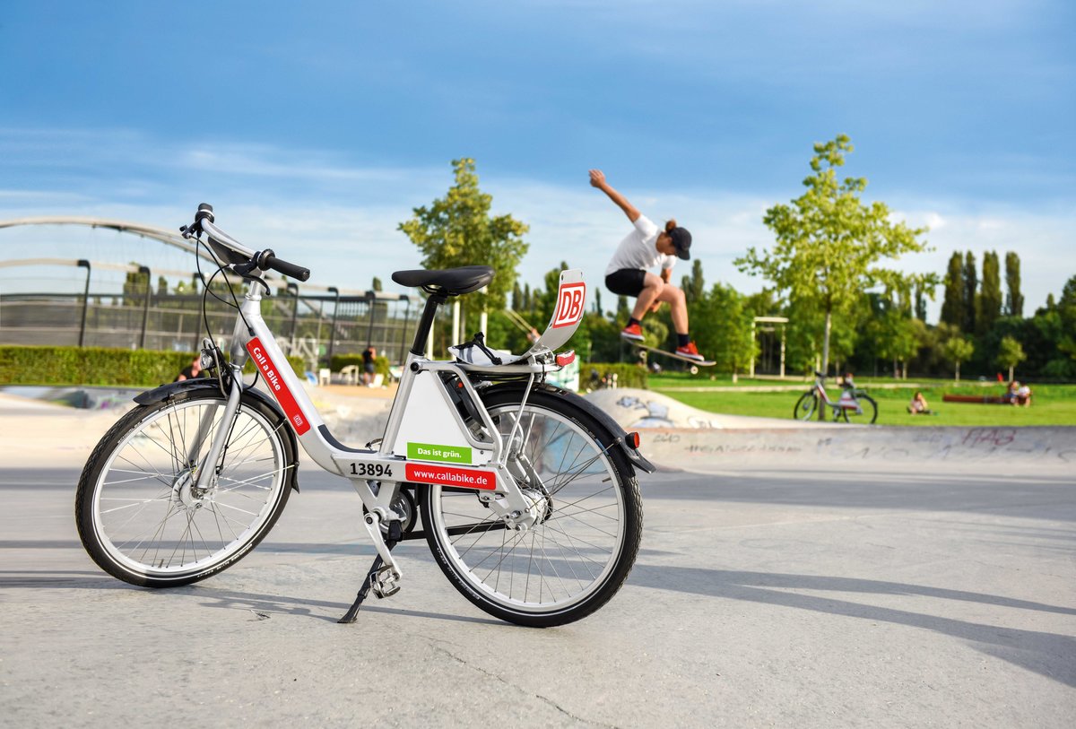 Ein Rad der Call a Bike-Initiative in einem Park, in dem ein junger Mann skatet.