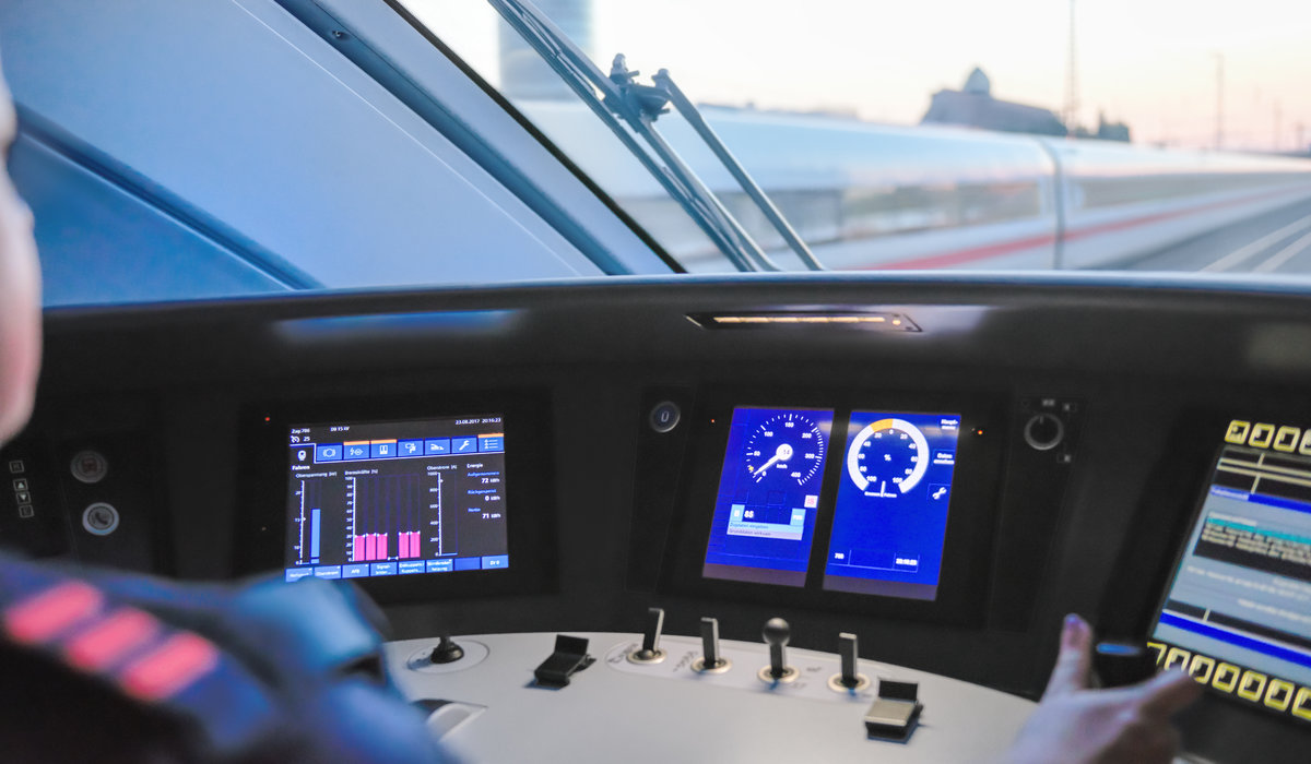 Blick auf drei verschiedene Monitore sowie die Steuerung im Führerhaus eines ICE. 