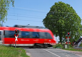 A red train crosses a level crossing in summer, the barriers are closed.