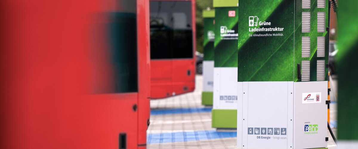 Eine grüne Ladesäule neben roten Elektro-Bussen am Bahnhof.  | © DB Energie GmbH / Max Lautenschläger