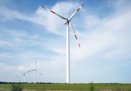 Windräder stehen auf einem Feld neben einer Gleisanlage.