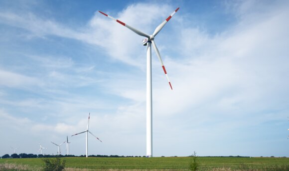 Windräder stehen auf einem Feld neben einer Gleisanlage.