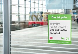 Am Bahnhof Südkreuz hängt das Signet für die Maßnahme Zukunftsbahnhof mit der Botschaft "Innovativ. Für die Umwelt. Der Zukunftsbahnhof.".