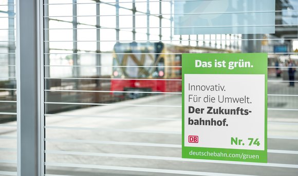 Am Bahnhof Südkreuz hängt das Signet für die Maßnahme Zukunftsbahnhof mit der Botschaft "Innovativ. Für die Umwelt. Der Zukunftsbahnhof.".
