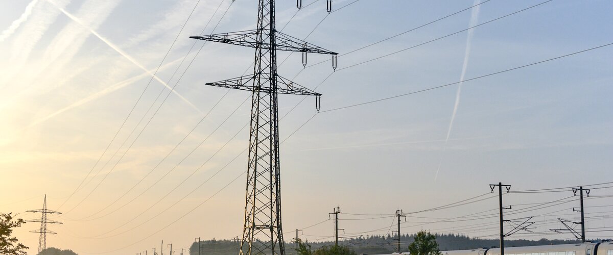 Ein Strommast steht neben einer Bahnstrecke auf einem Feld. | © DB AG / Volker Emersleben