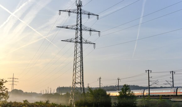 Ein Strommast steht neben einer Bahnstrecke auf einem Feld.