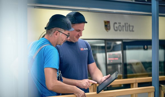 Zwei Mitarbeiter arbeiten am Bahnhof mit einem Tablet.