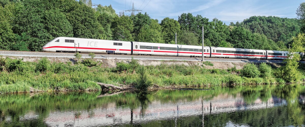 Ein ICE fährt entlang eines Flusses durch eine grüne Landschaft. | © Barteld Redaktion & Verlag