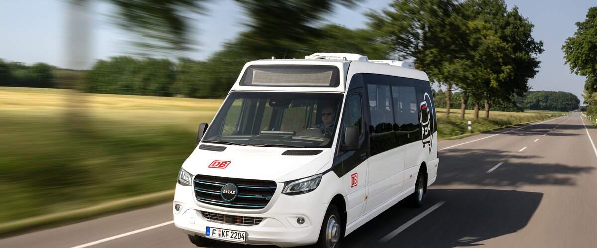 A white minibus with DB branding drives along a country road.