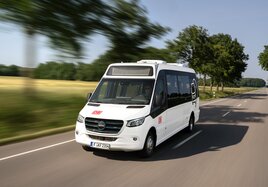 Ein weißer Minibus mit DB Branding fährt auf einer Landstraße.