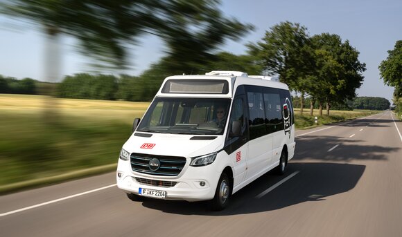 A white minibus with DB branding drives along a country road.