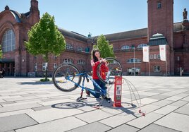 Eine Frau repariert auf dem Bahnhofsvorplatz ihr Rad an einer der mobilen Reparatursäulen bei DB Station&Service. 