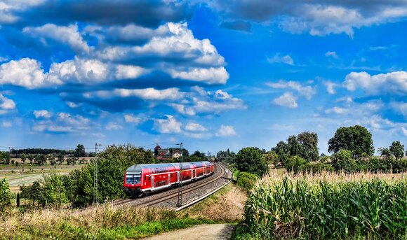 Ein Zug der Deutschen Bahn fährt vorbei an Feldern durch die Natur. 