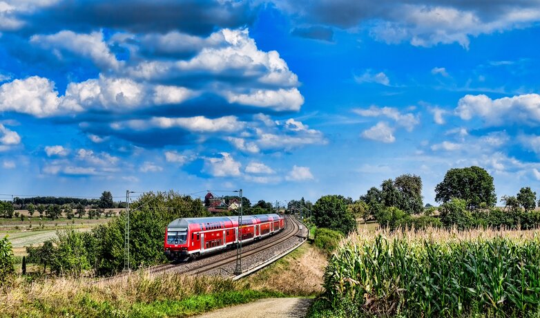 Ein Zug der Deutschen Bahn fährt vorbei an Feldern durch die Natur.  | © Andre Bull