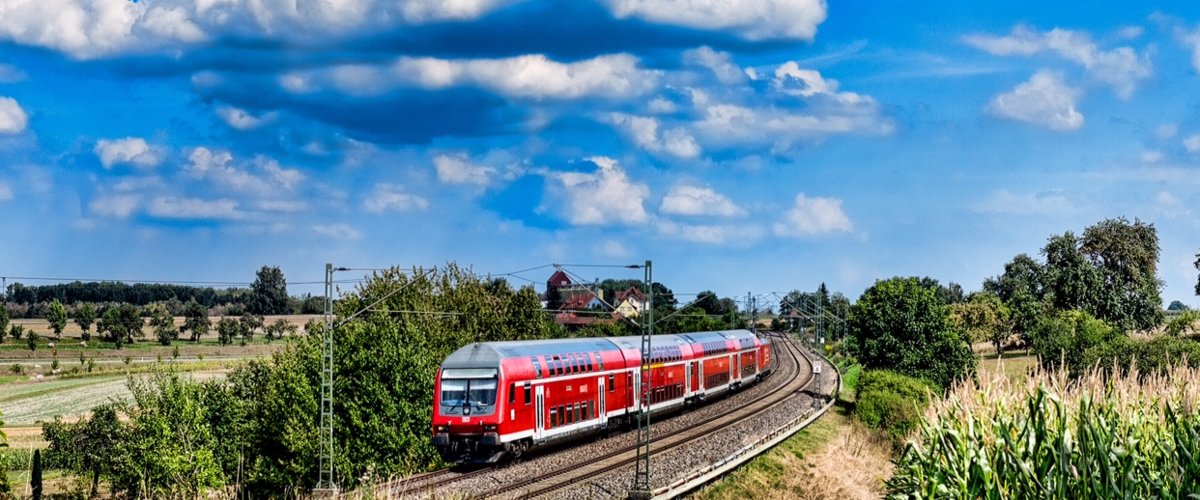 Ein Zug der Deutschen Bahn fährt vorbei an Feldern durch die Natur.  | © Andre Bull