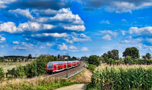 Ein Zug der Deutschen Bahn fährt vorbei an Feldern durch die Natur. 