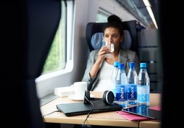 In einem DB-Zug trinkt eine Reisende Wasser aus einer share-Flasche.