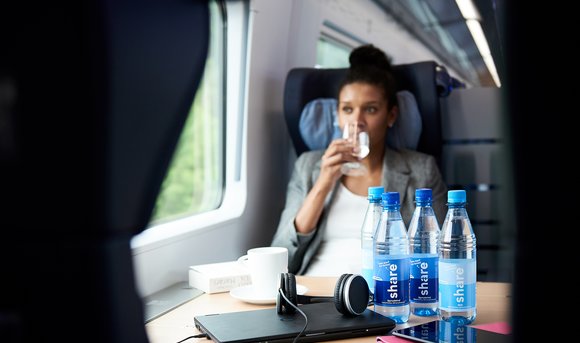 In einem DB-Zug trinkt eine Reisende Wasser aus einer share-Flasche.
