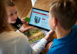 Eine Familie durchstöbert auf dem Tablet die BahnBonus Prämienwelt nach den nachhaltigen Produkten und Dienstleistungen.