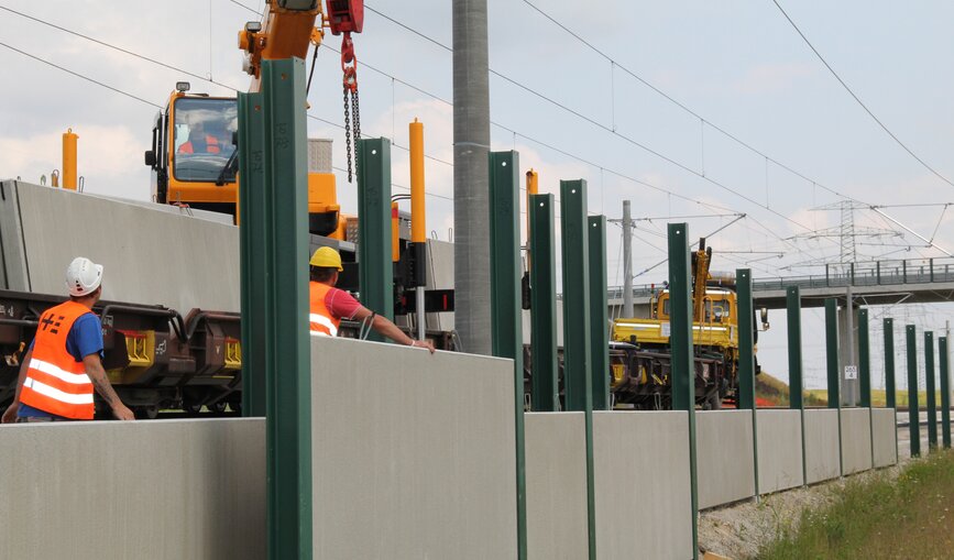 DB-Mitarbeiter errichten Lärmschutzwände an einer Bahnstrecke. 