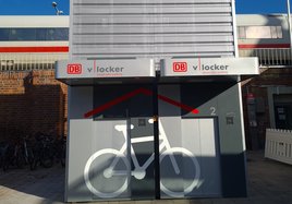 Zwei automatisierte Fahrradparkhäuser für insgesamt zwölf Räder stehen vor dem Zukunftsbahnhof in Halle (Saale). Im Hintergrund fährt ein Zug vorbei.