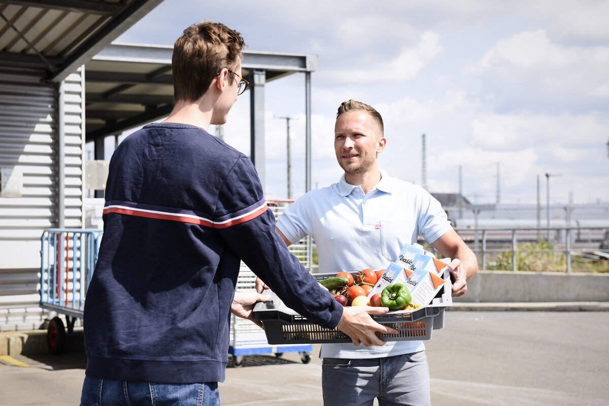 Ein DB-Mitarbeiter übergibt einen Korb mit Lebensmitteln einem Tafel-Mitarbeiter. | © DB AG / Faruk Hosseini