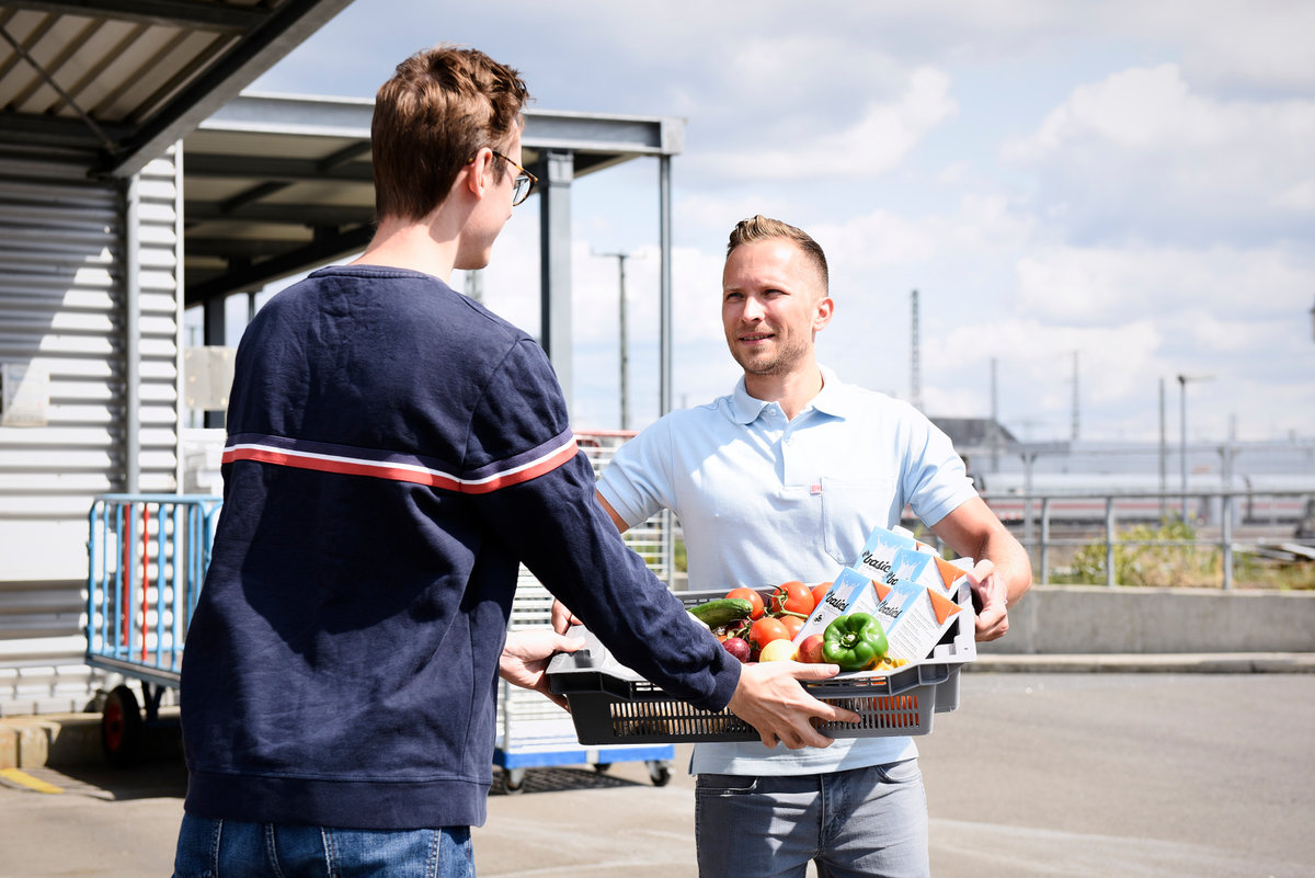 Ein DB-Mitarbeiter übergibt einen Korb mit Lebensmitteln einem Tafel-Mitarbeiter.