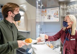 Eine Mitarbeiterin des Bordbistros serviert einem Bahnkunden seine Bestellung auf Porzellangeschirr