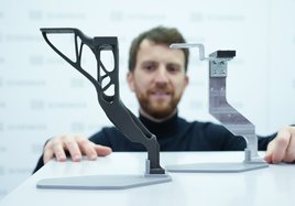 Ein Mann zeigt ein Ersatzteil aus dem 3D-Drucker.