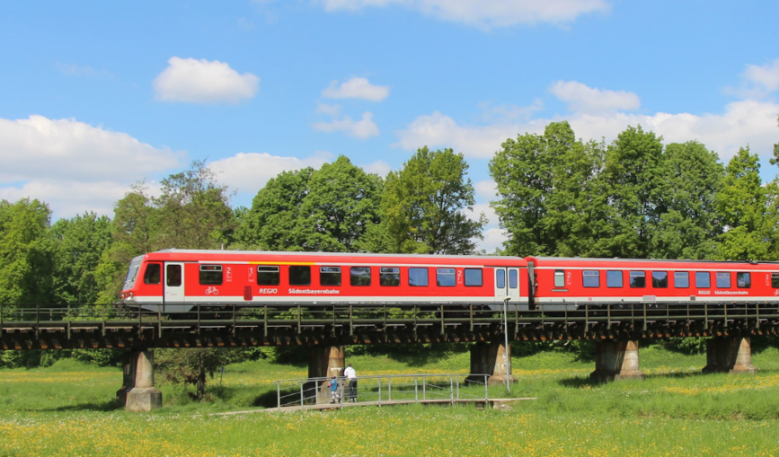 Ein Zug der Südostbayernbahn fährt durch eine grüne Landschaft.