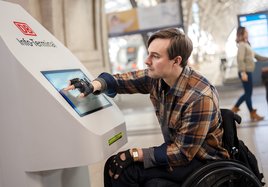 Ein Rollstuhlfahrer an einem DB Info-Terminal in der Bahnhofshalle des Hauptbahnhofs Leipzig.