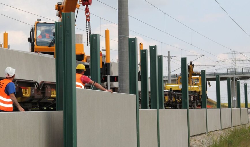 Bauarbeiter errichten Lärmschutzwände an einer Bahnstrecke