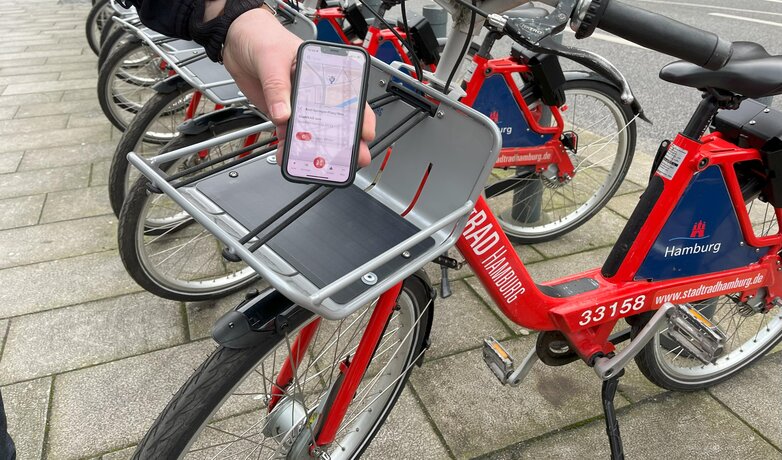 DB AG / Angelika Theidig | © Eine Person zeigt die StadtRAD Hamburg App auf ihrem Smartphone. Im Hintergrund stehen StadtRAD HAmburg Fahrräder.