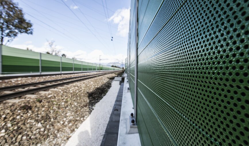 Eine grüne Lärmschutzwand entlang der Gleise