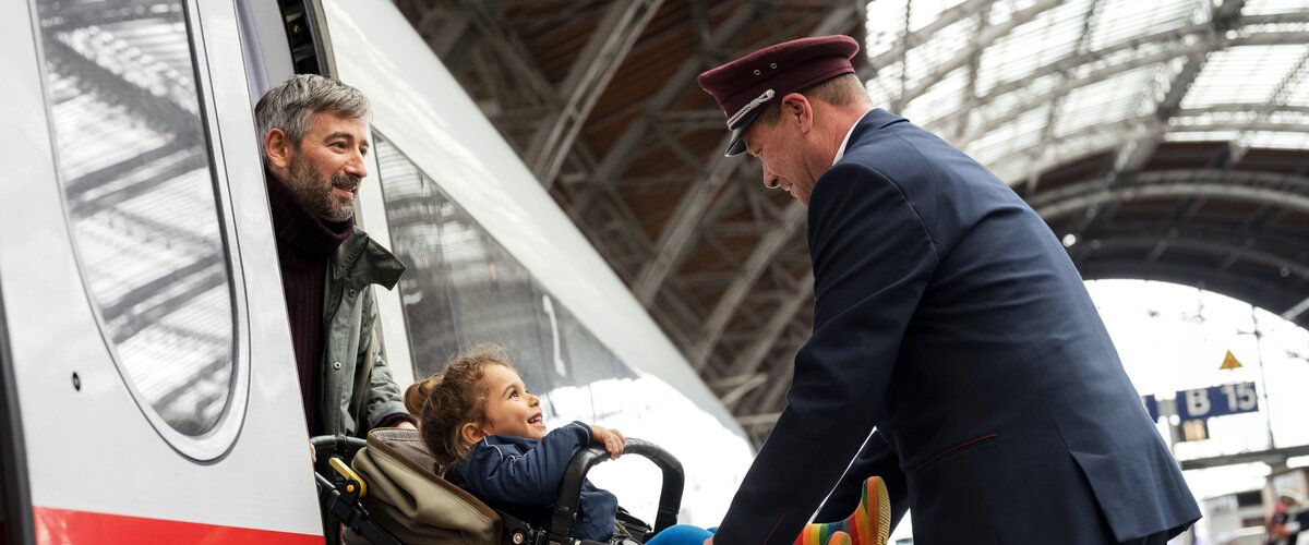 Eine DB Servicekraft hilft einem Vater mit Kinderwagen beim Einstieg in einen ICE. | © DB AG / Max Lautenschläger