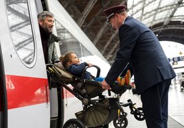 Eine DB Servicekraft hilft einem Vater mit Kinderwagen beim Einstieg in einen ICE.