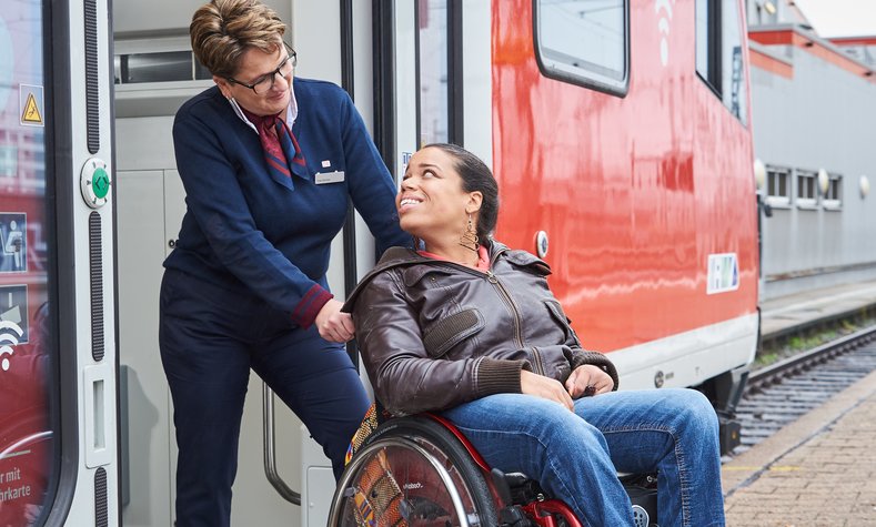 Eine Zugbegleiterin hilft einer Frau im Rollstuhl beim Einstieg in einen Regionalzug.