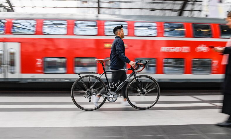 Ein Mann schiebt ein Fahrrad an einem Bahnsteig.