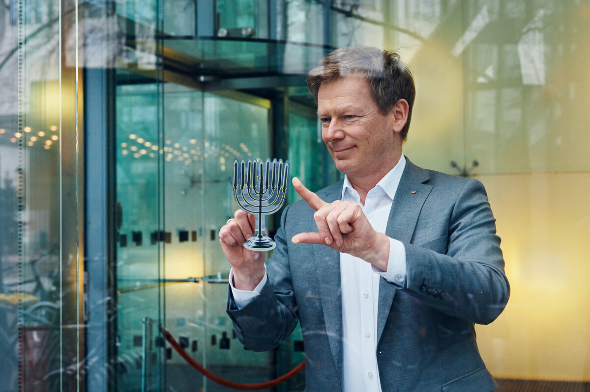 Richard Lutz, DB-Vorstandsvorsitzender, befestigt einen Aufkleber des Chanukka-Leuchters in der DB Konzernzentrale. | © Deutsche Bahn AG / Dominic Dupont