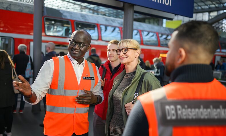 Ein Mitarbeitender der DB Sicherheit erklärt Reisenden den Weg