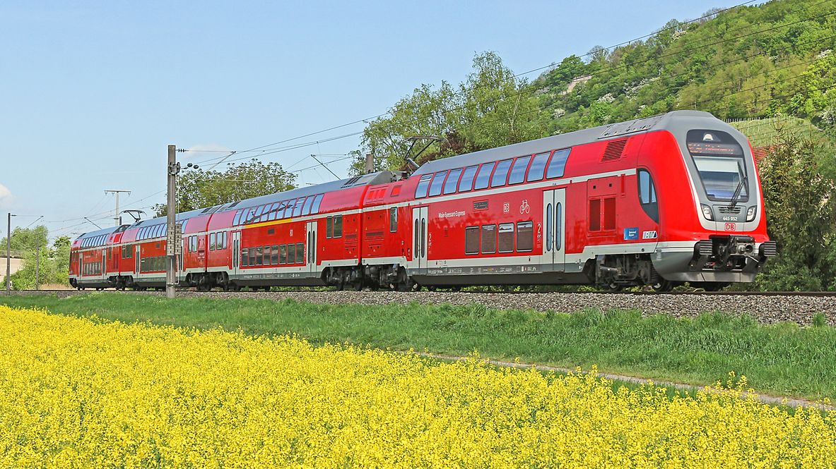 Ein roter Regionalzug der Deutschen Bahn fährt durch die Natur vorbei an einem gelb-blühenden Rapsfeld.