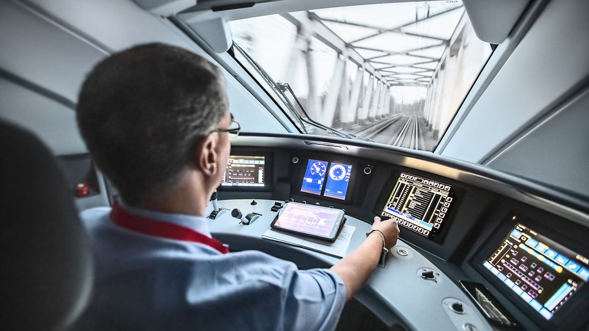 Ein Lokführer steuert den ICE und blickt dabei durch die Frontscheibe auf die Strecke.
