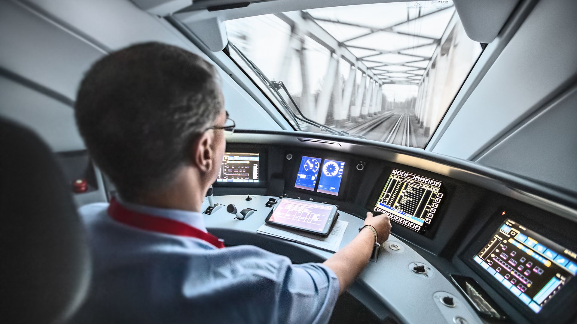 Ein Lokführer steuert den ICE und blickt dabei durch die Frontscheibe auf die Strecke.