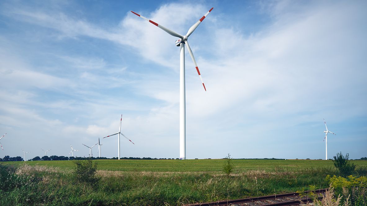 Windräder stehen auf einem Feld neben einer Gleisanlage.